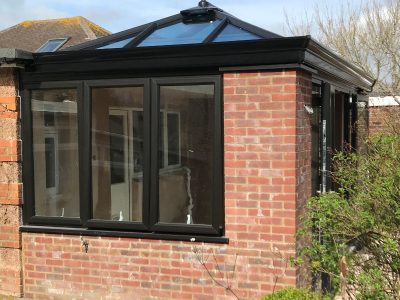 Bespoke build orangery in Eastbourne garden with black windows, French doors and lantern on the roof. Side view from the pond